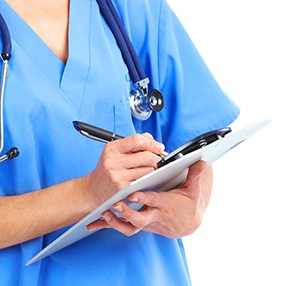 Medical professional in blue scrubs writing on a clipboard